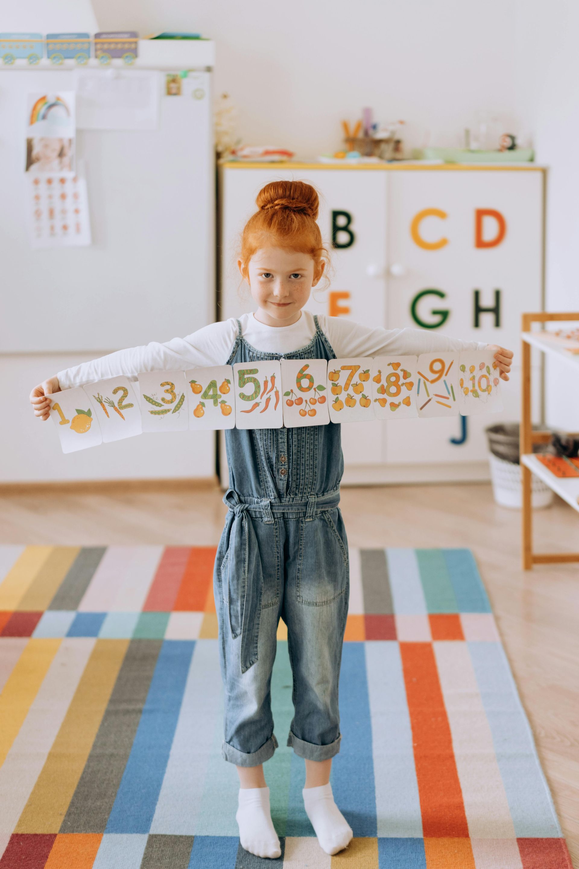 Child holding a number chain in a colorful classroom with alphabet blocks and a striped rug