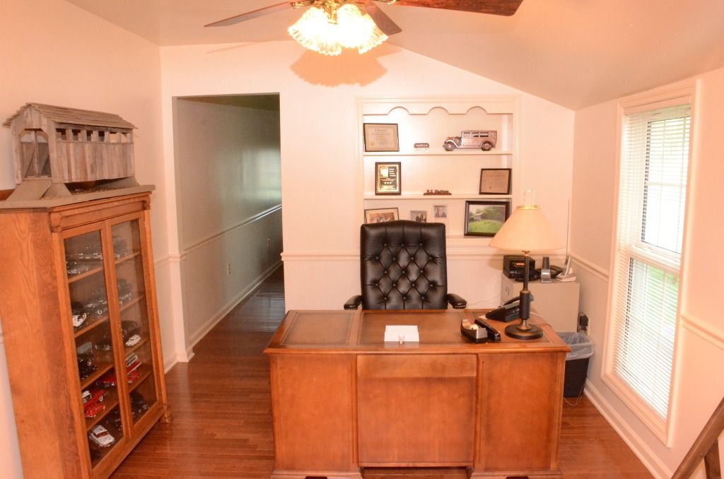 A home office featuring a wooden desk, a black leather office chair, a display cabinet, and a built-in bookshelf.