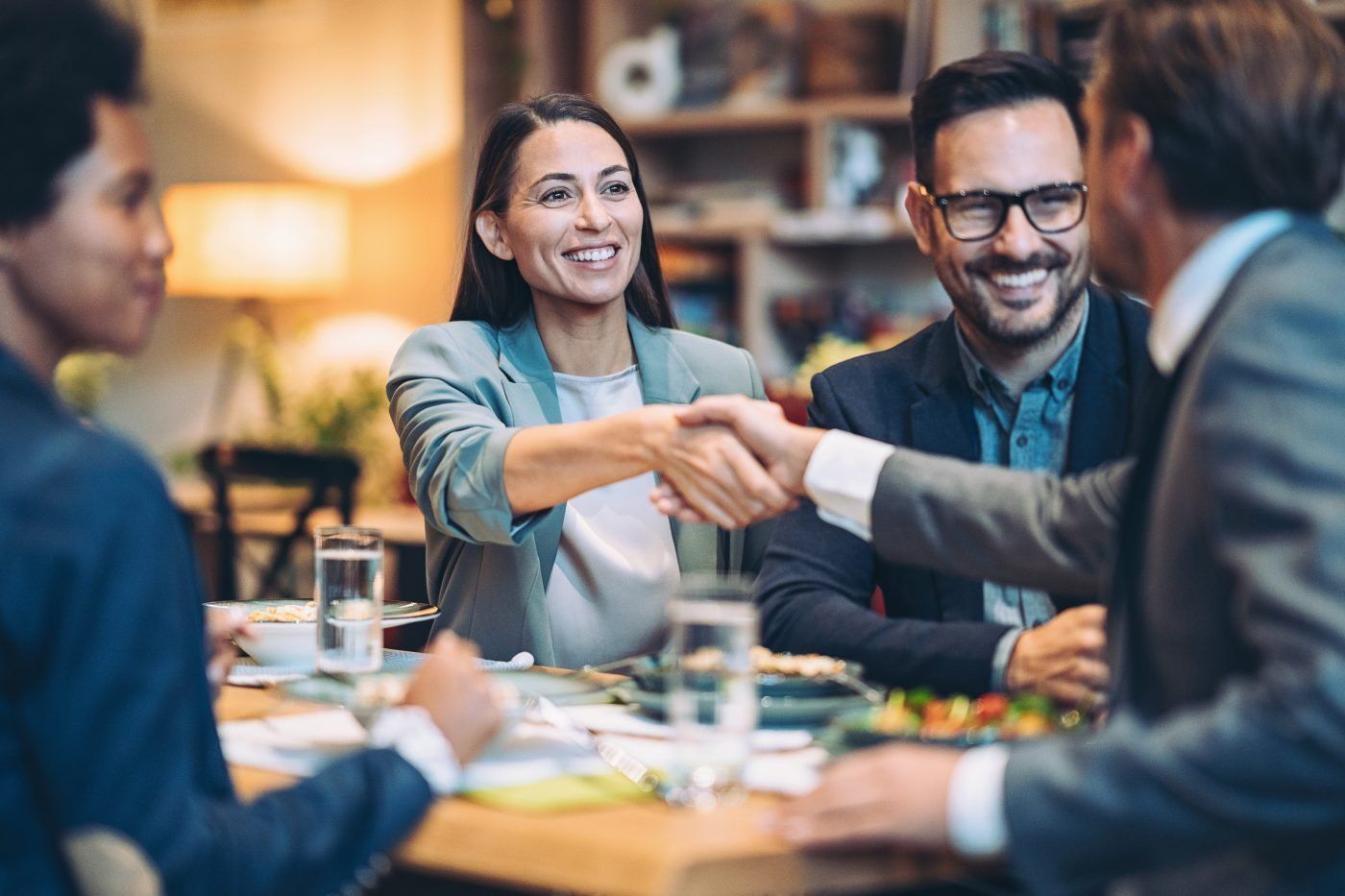 a group of people are sitting at a table shaking hands .