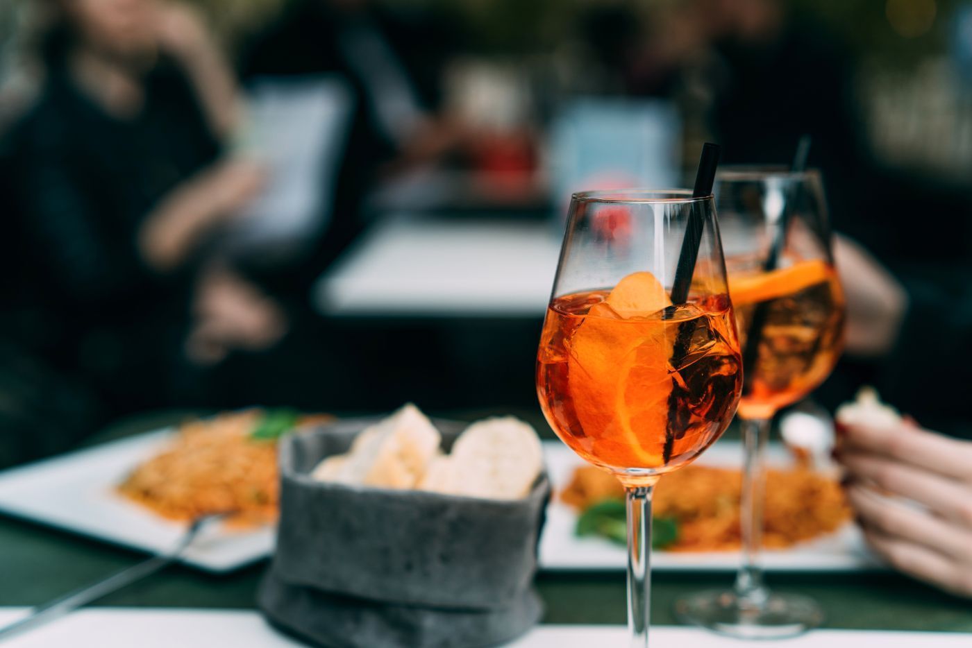 two glasses of orange juice with straws on a table with plates of food .