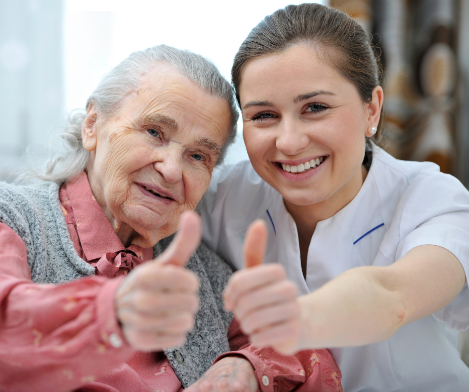 Elderly woman and caregiver smiling with thumbs up.