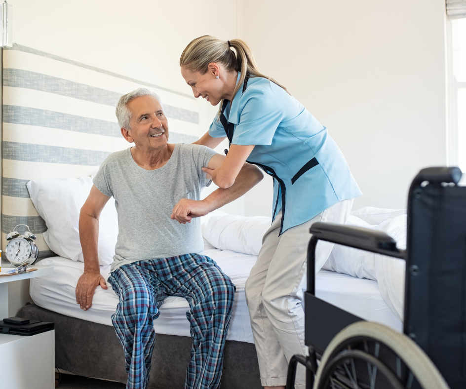 A healthcare worker assists a person sitting on a bed, with a wheelchair nearby.