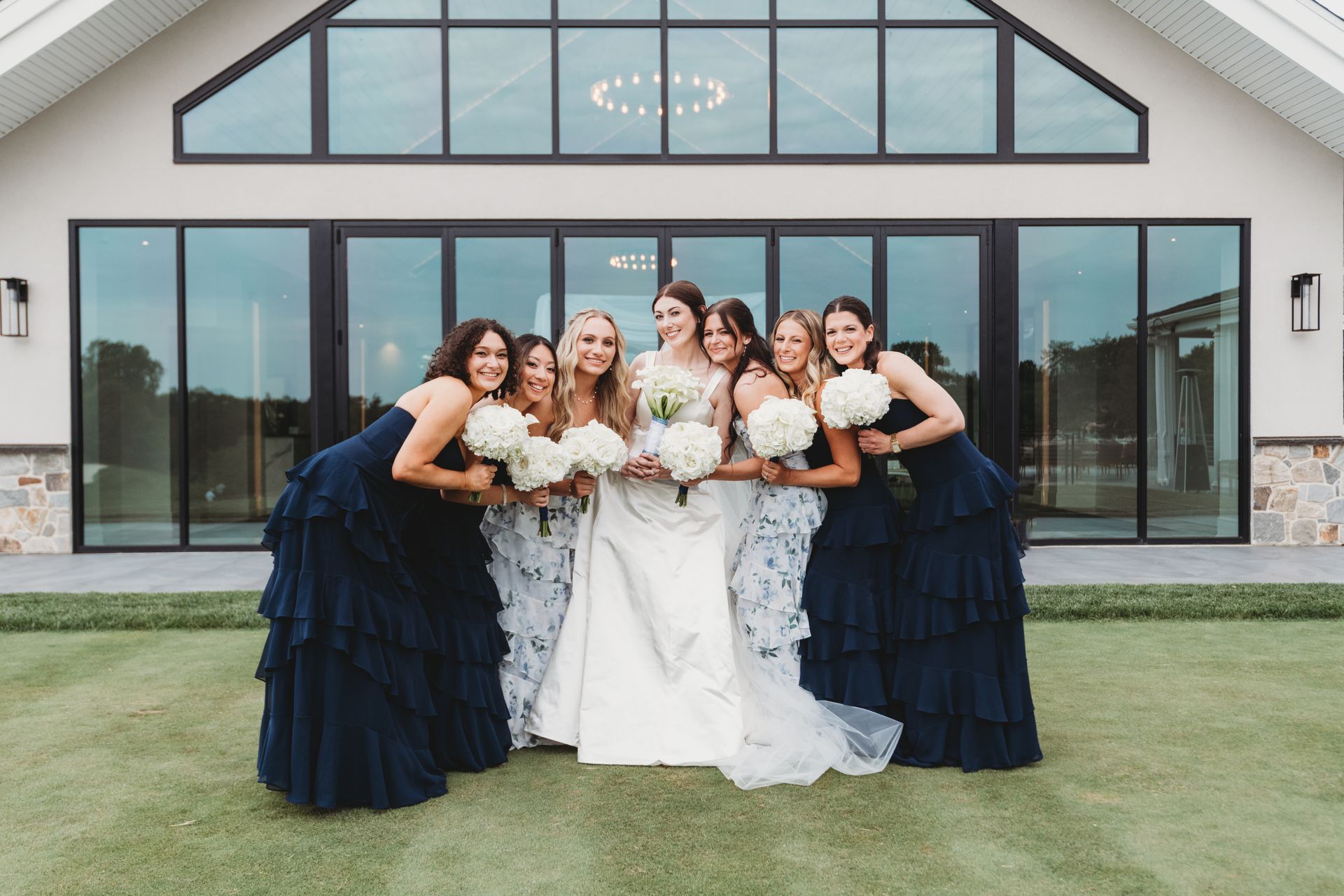 Group of women in dark blue and white dresses posing in front of a modern glass building