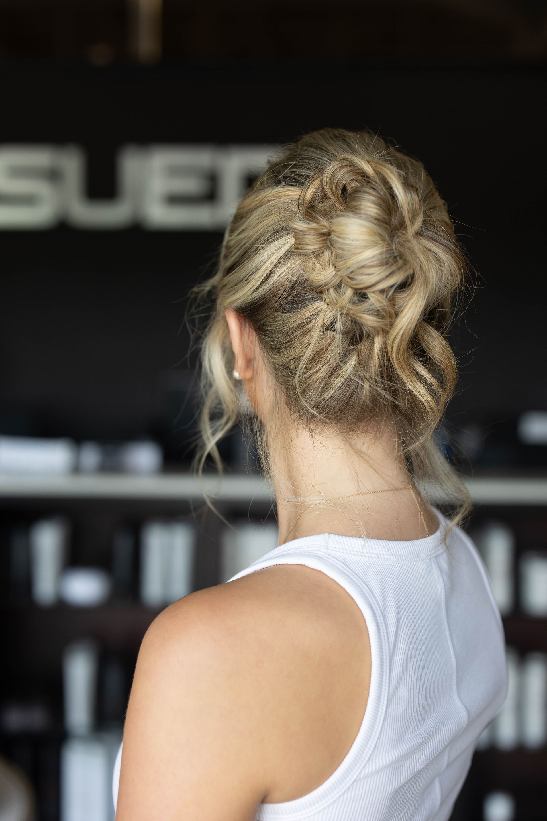 Woman with blonde hair in a white tank top seen from behind