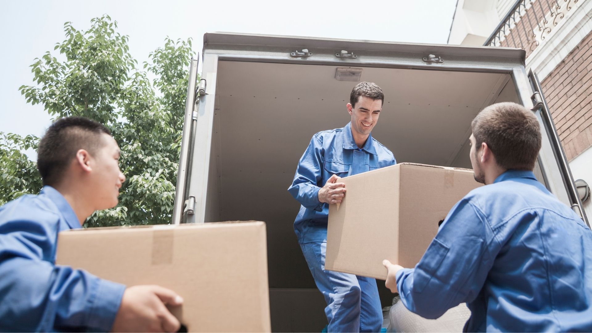 Movers in blue uniforms loading cardboard boxes into a truck.