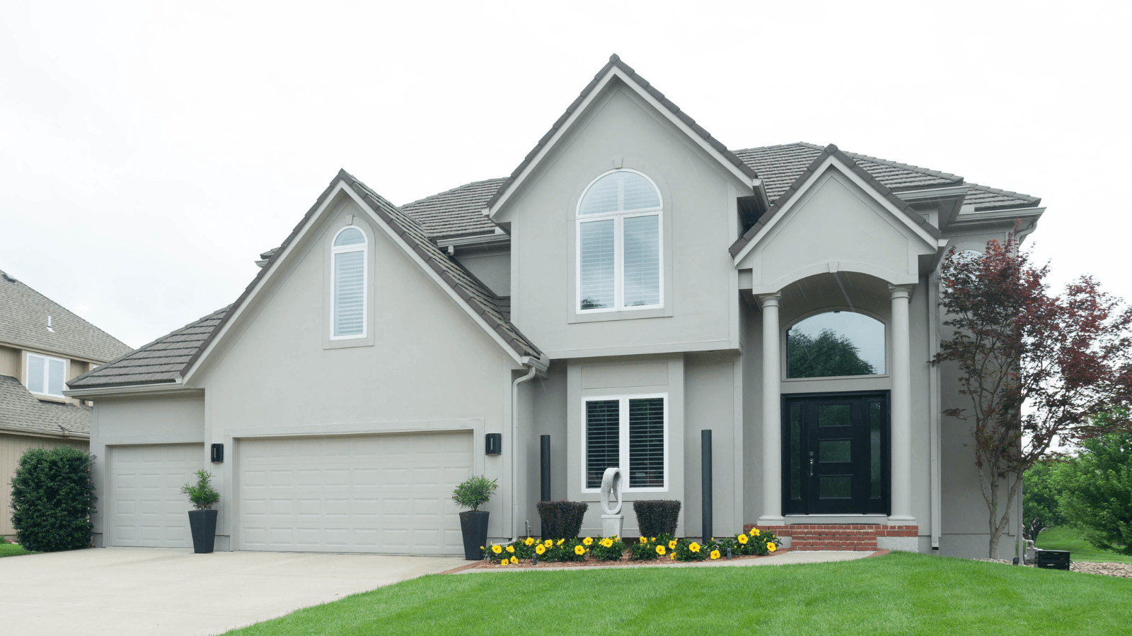 Light grey two-story house with a grey tile roof, two-car garage, and green lawn.