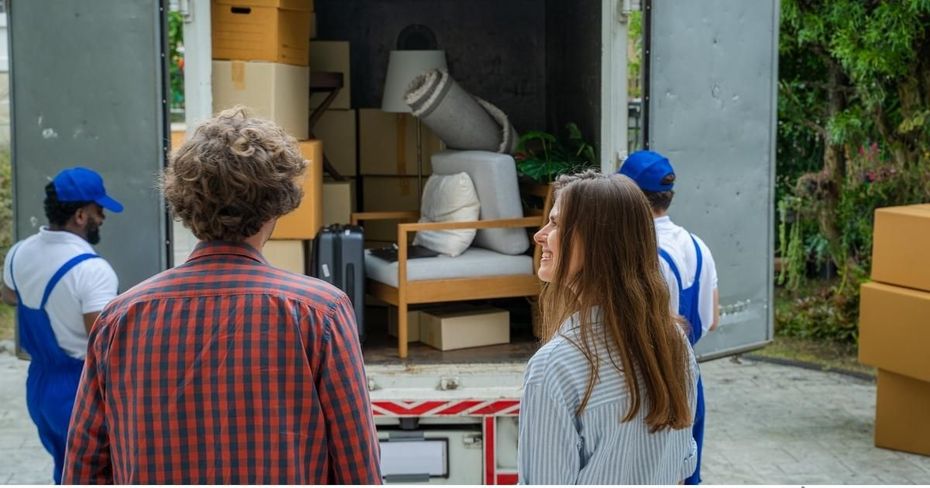 People standing by a moving truck, watching furniture being unloaded from the back.