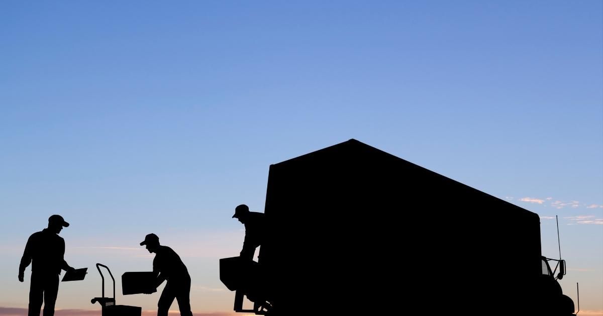 Silhouetted workers loading a truck against a blue and orange sky.