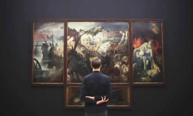 Man facing a triptych painting in a dimly lit museum. The artwork depicts a chaotic battle scene with dark hues.