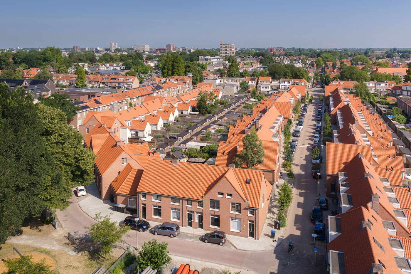 Luchtfoto van een woonwijk met huizen met oranje daken en met bomen omzoomde straten onder een heldere hemel