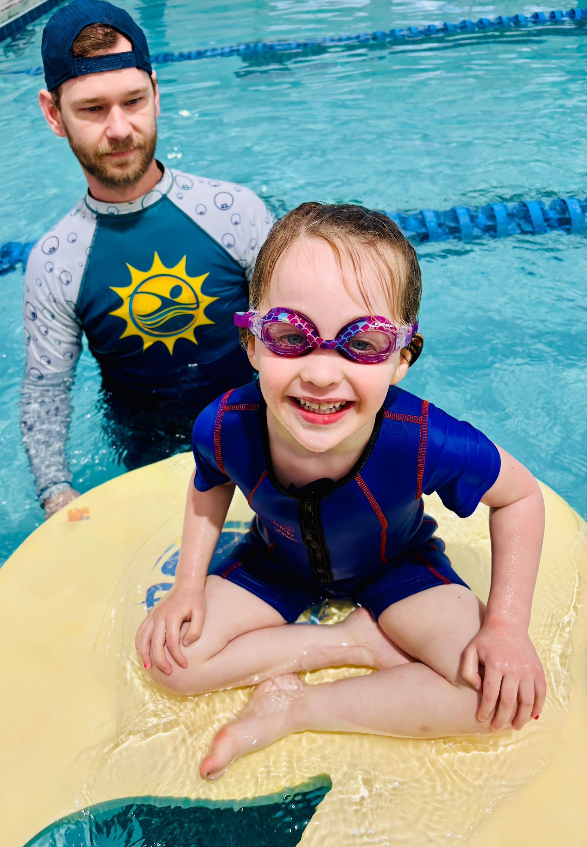 A swim instructor guiding a child floating on a pool device.