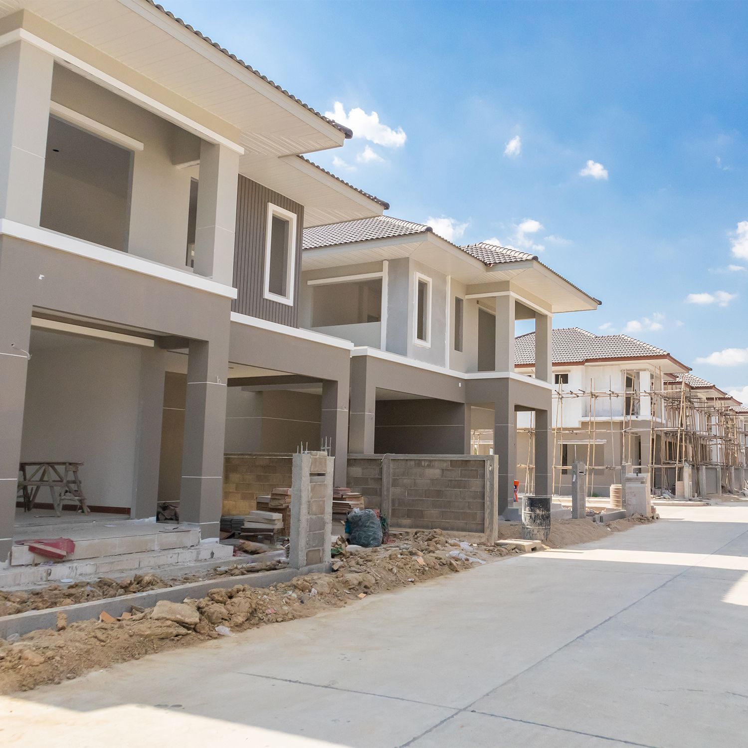 Hilera de casas en construcción en un día soleado. Exteriores grises y blancos, entradas abiertas, cielo azul.