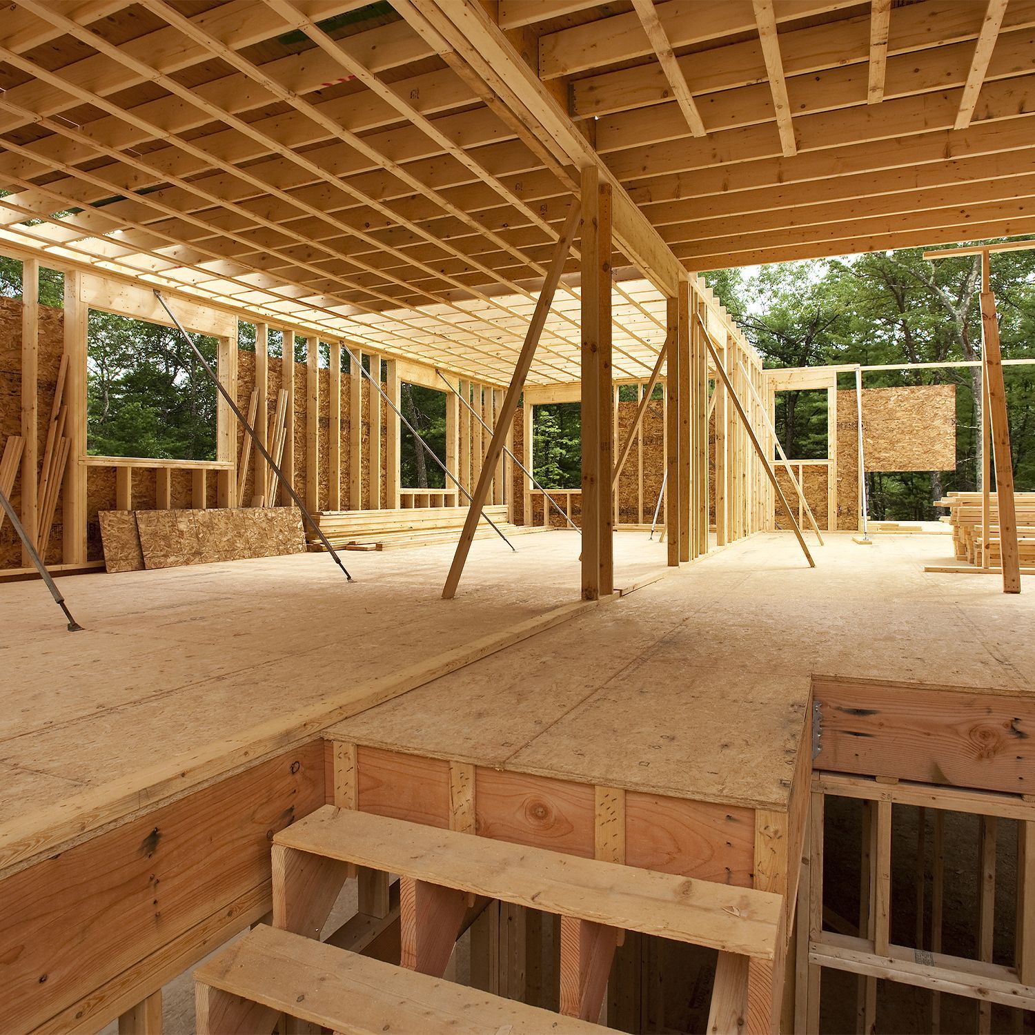 Casa de madera en construcción; estructura expuesta, escaleras, ventanas, vigas de soporte; vista interior.