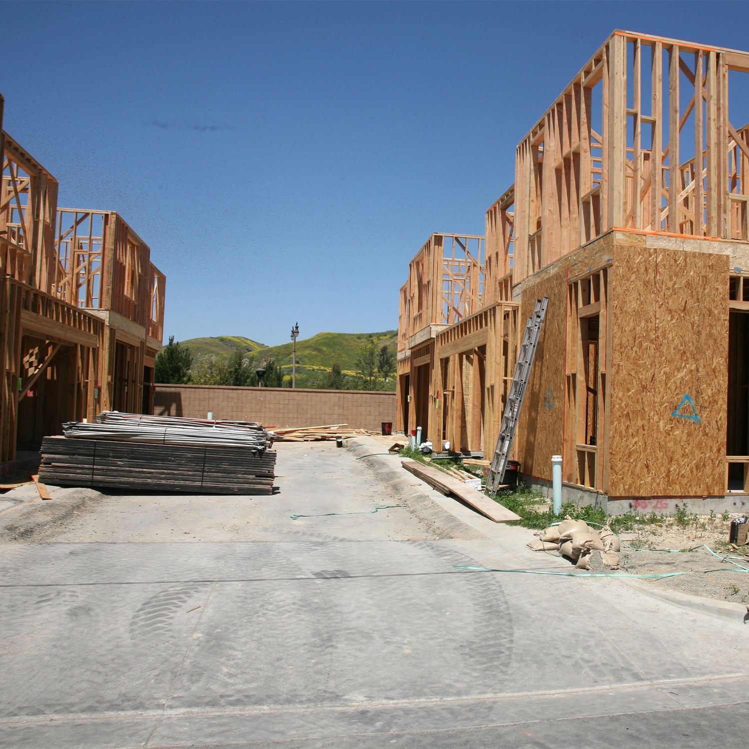 Sitio de construcción con marcos de madera para casas adosadas, un camino pavimentado y un cielo azul claro.