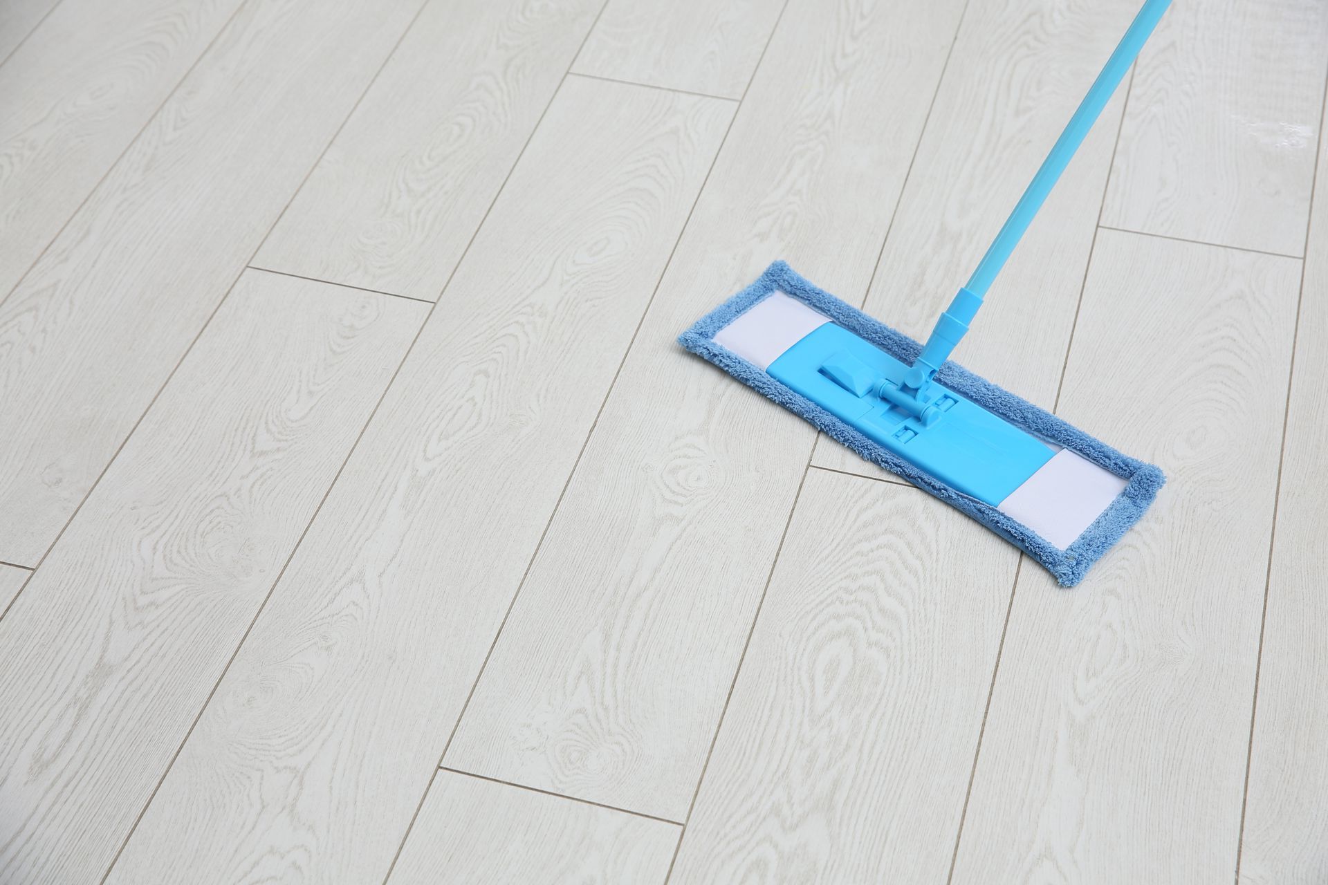 Fregona azul limpiando un piso de madera de color claro.