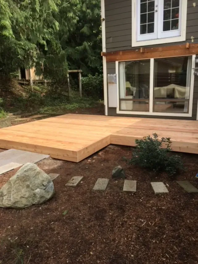 Wooden deck adjacent to a house, with landscaping including rocks and stepping stones.