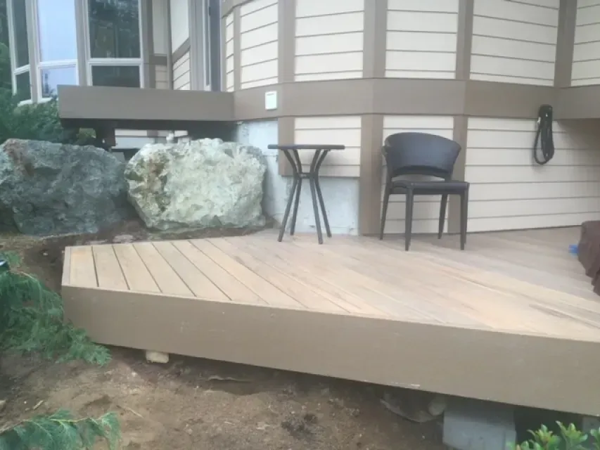 A deck with composite decking, a small table and chair, and a large boulder in a residential outdoor setting.