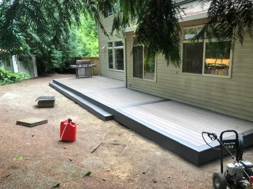 Deck with steps, a grill, and a gas can in a backyard setting next to a light beige house.