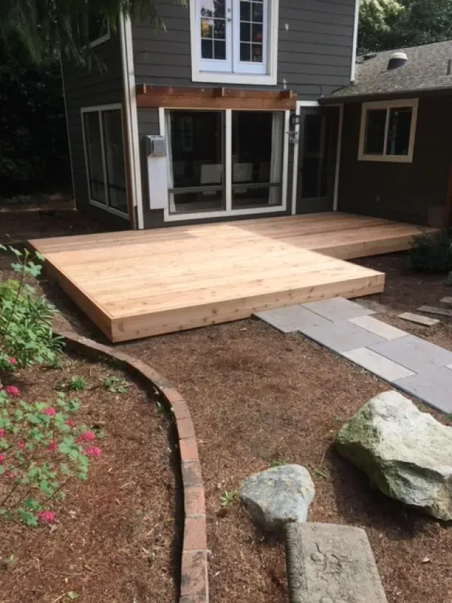 Newly built wooden deck outside a two-story house with a pathway and garden.