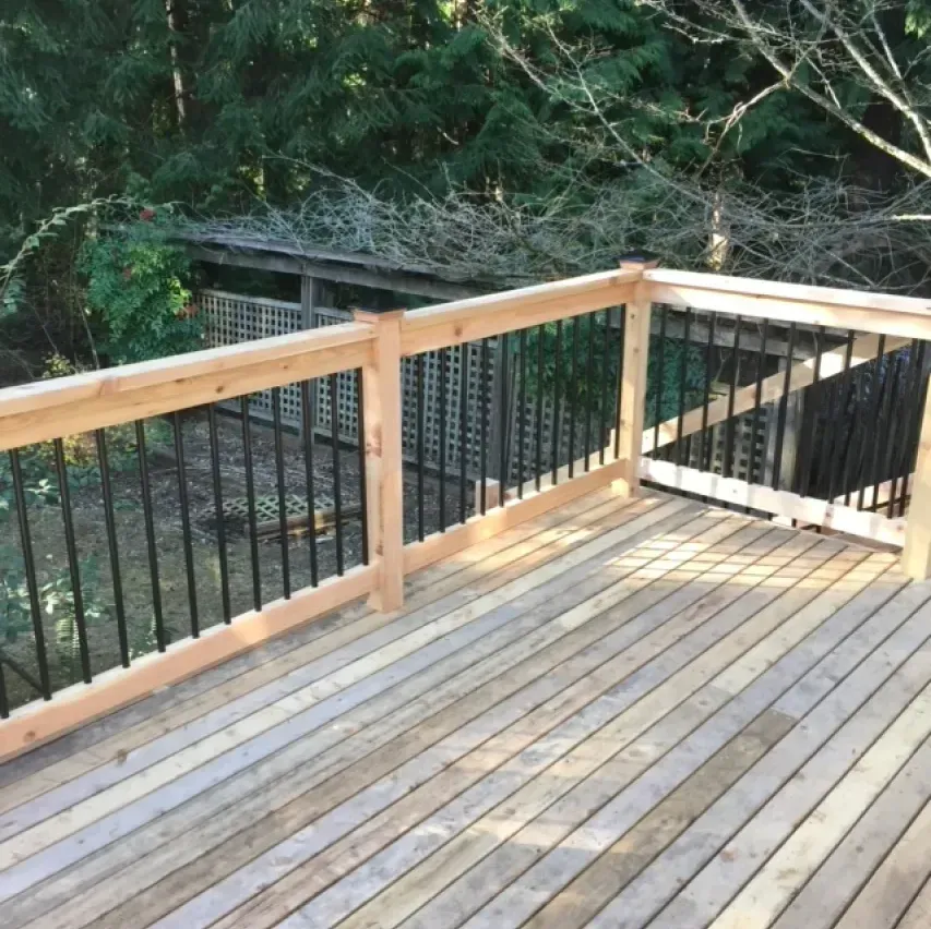 Wooden deck with black railing and wood posts, overlooking a wooded area.