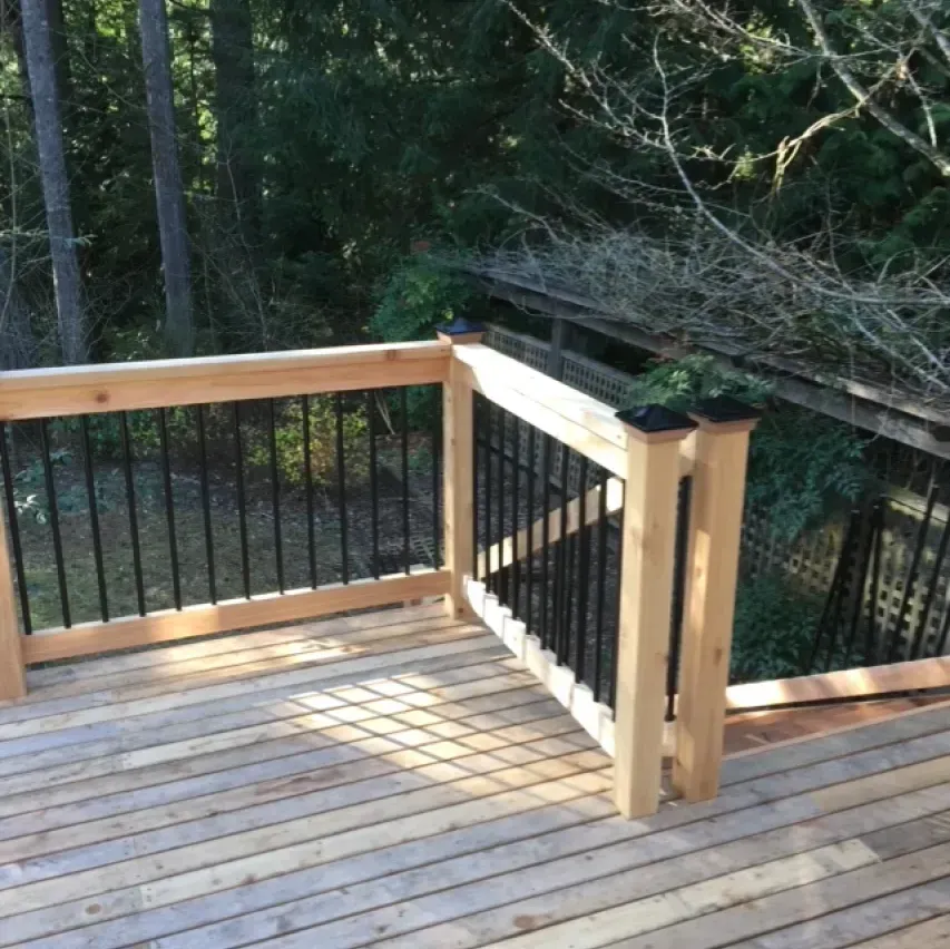 Wooden deck with black railings and light-colored wooden posts, overlooking a wooded area.