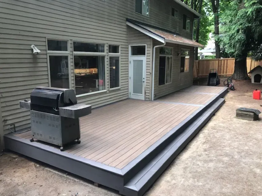 Backyard deck with a grill and access to a house. Wooden deck with a gray frame.