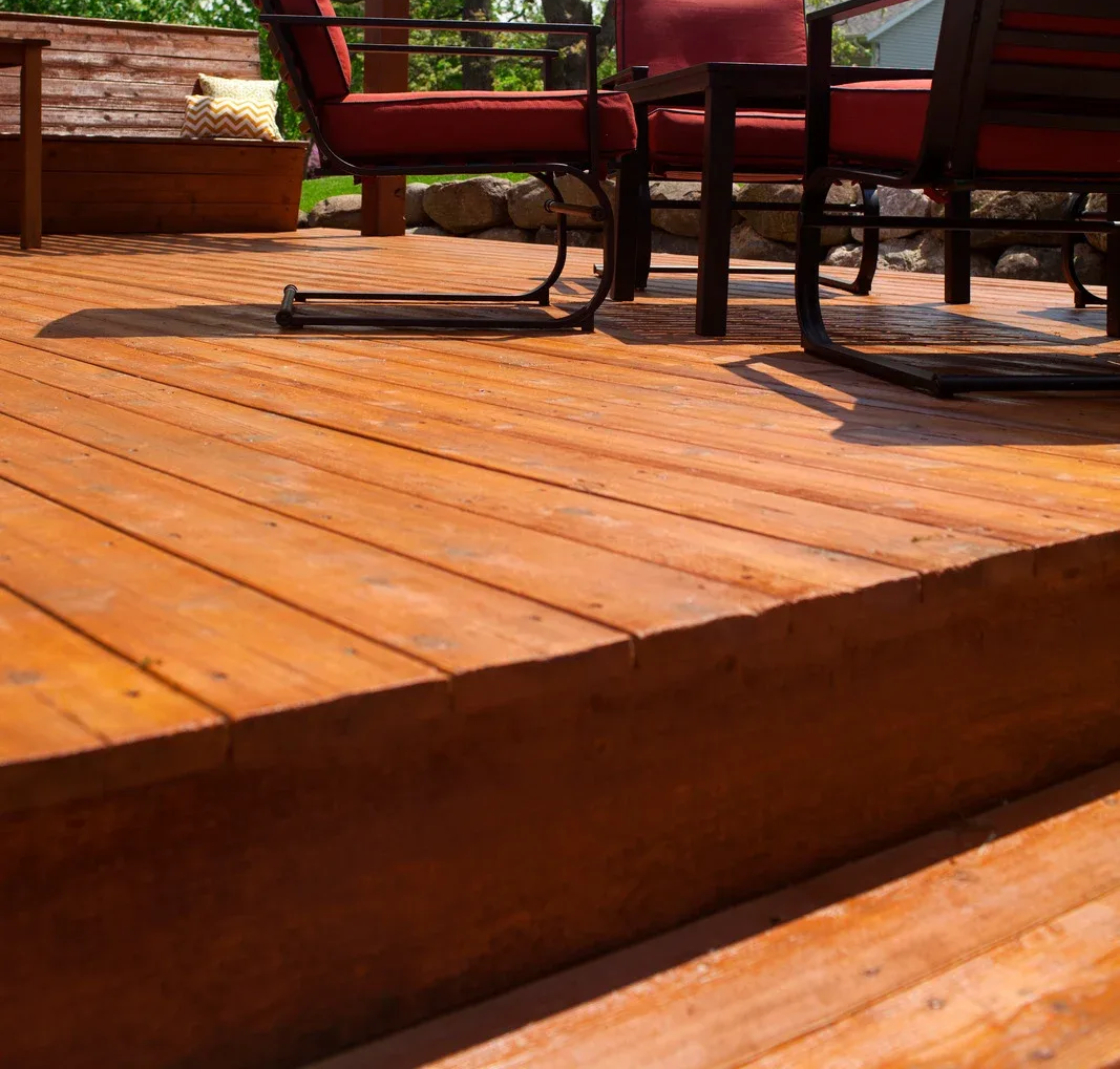 Wooden deck with red chairs and a table in a sunlit outdoor setting.