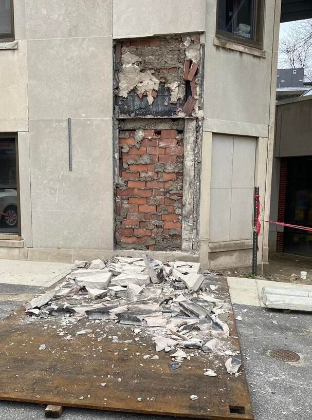 Part of a concrete faceade broken and falling away, exposing the brick underneath