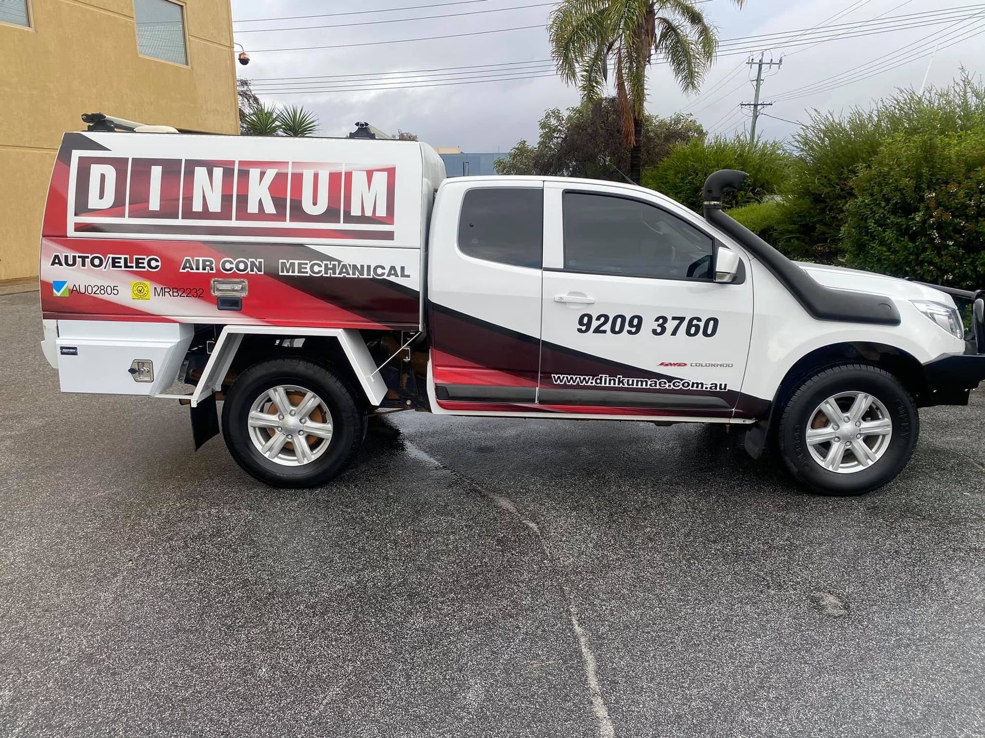 White utility truck with DINKUM signage parked on wet pavement under an overcast sky