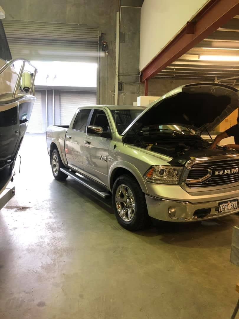 Silver pickup truck with hood open inside a garage, beside another vehicle near a large door