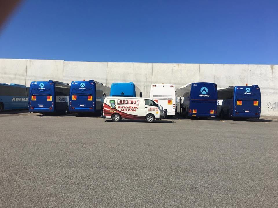 White van parked between blue trucks in a lot under a clear blue sky White van parked between blue trucks in a lot under a clear blue sky