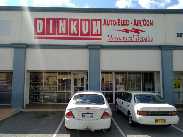 Auto repair shop storefront with two parked cars and a DINKUM sign.