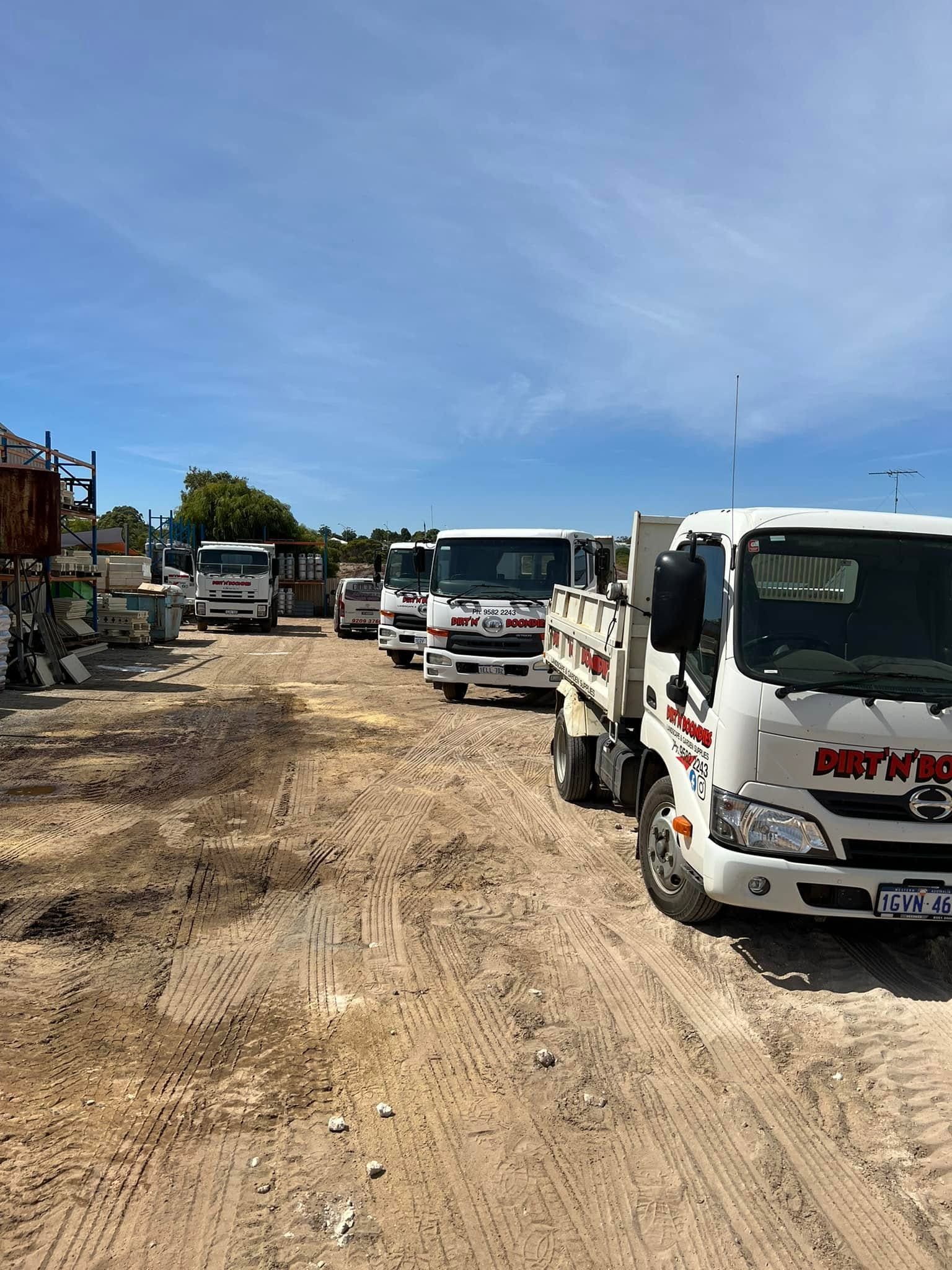 Row of white buses and vans parked on a muddy dirt road under a bright blue sky Row of white buses and vans parked on a muddy dirt road under a bright blue sky