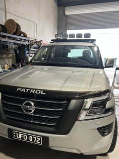 White Nissan Patrol SUV parked in a garage, front view with license plate visible.