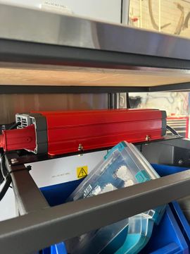 Red industrial machine above a blue bin with a clear plastic package inside.