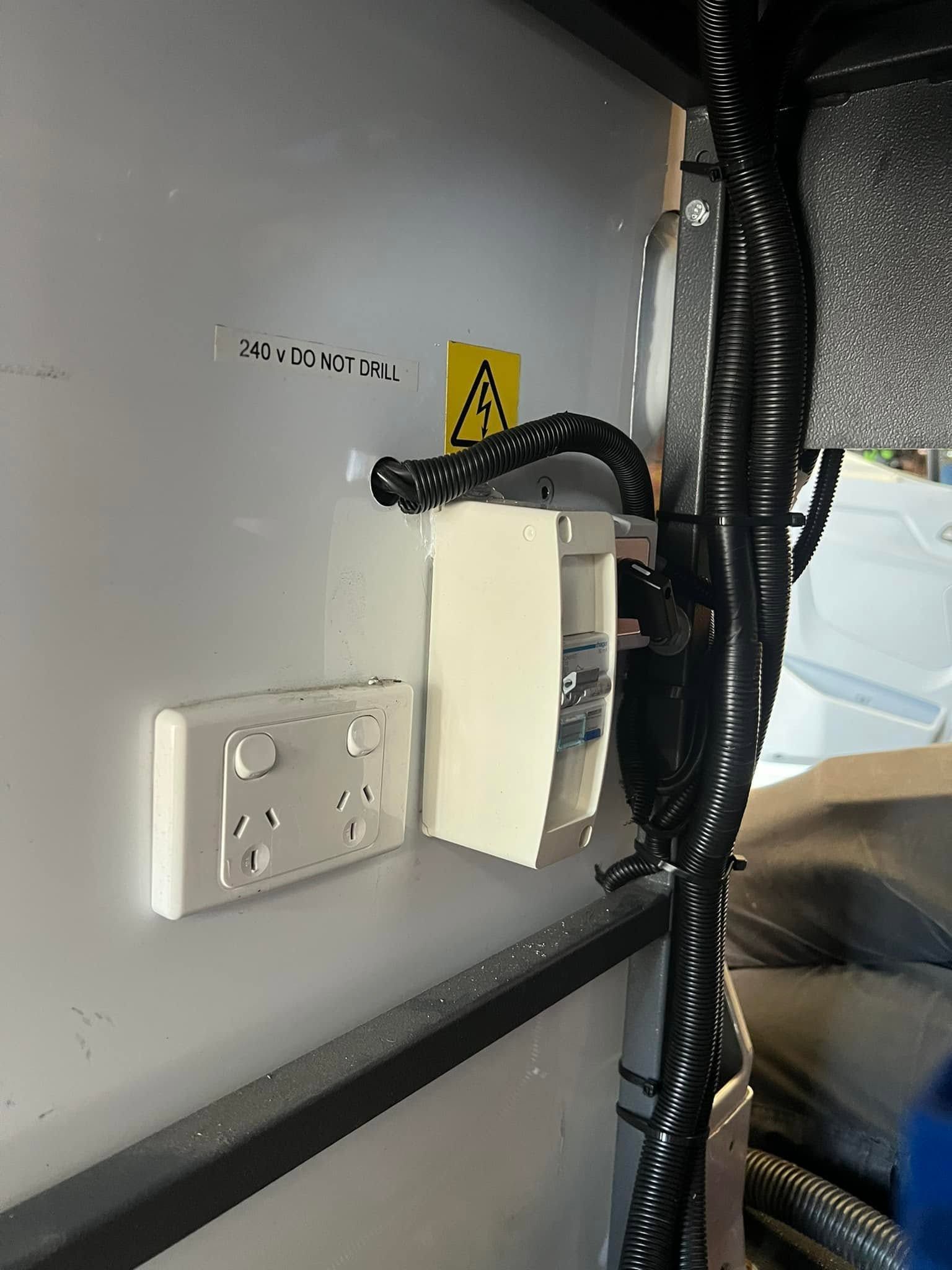 Electrical outlet and mounted device with cables inside a gray vehicle compartment.