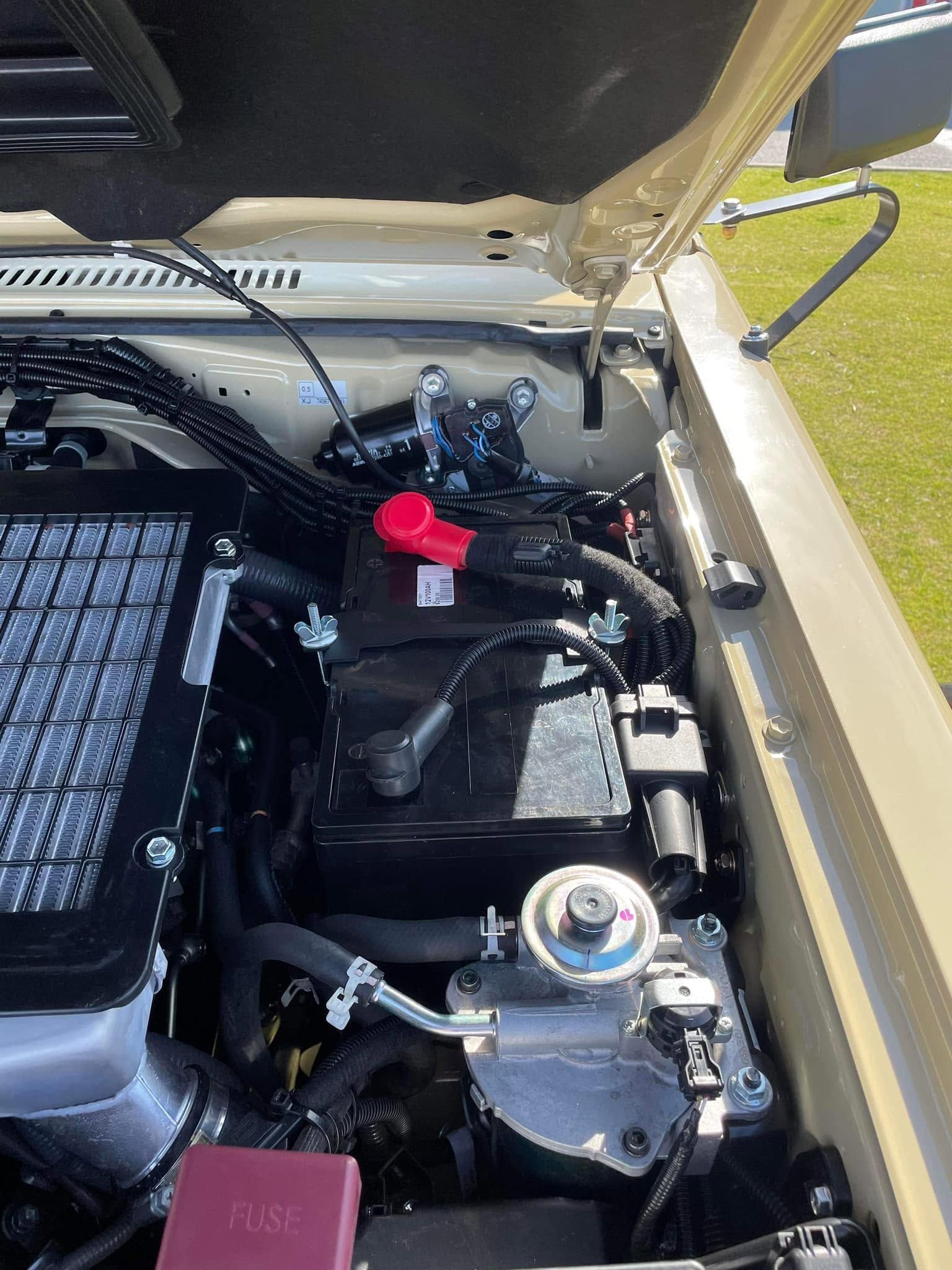 Open car hood showing an engine bay with black components and a red cap near the windshield.