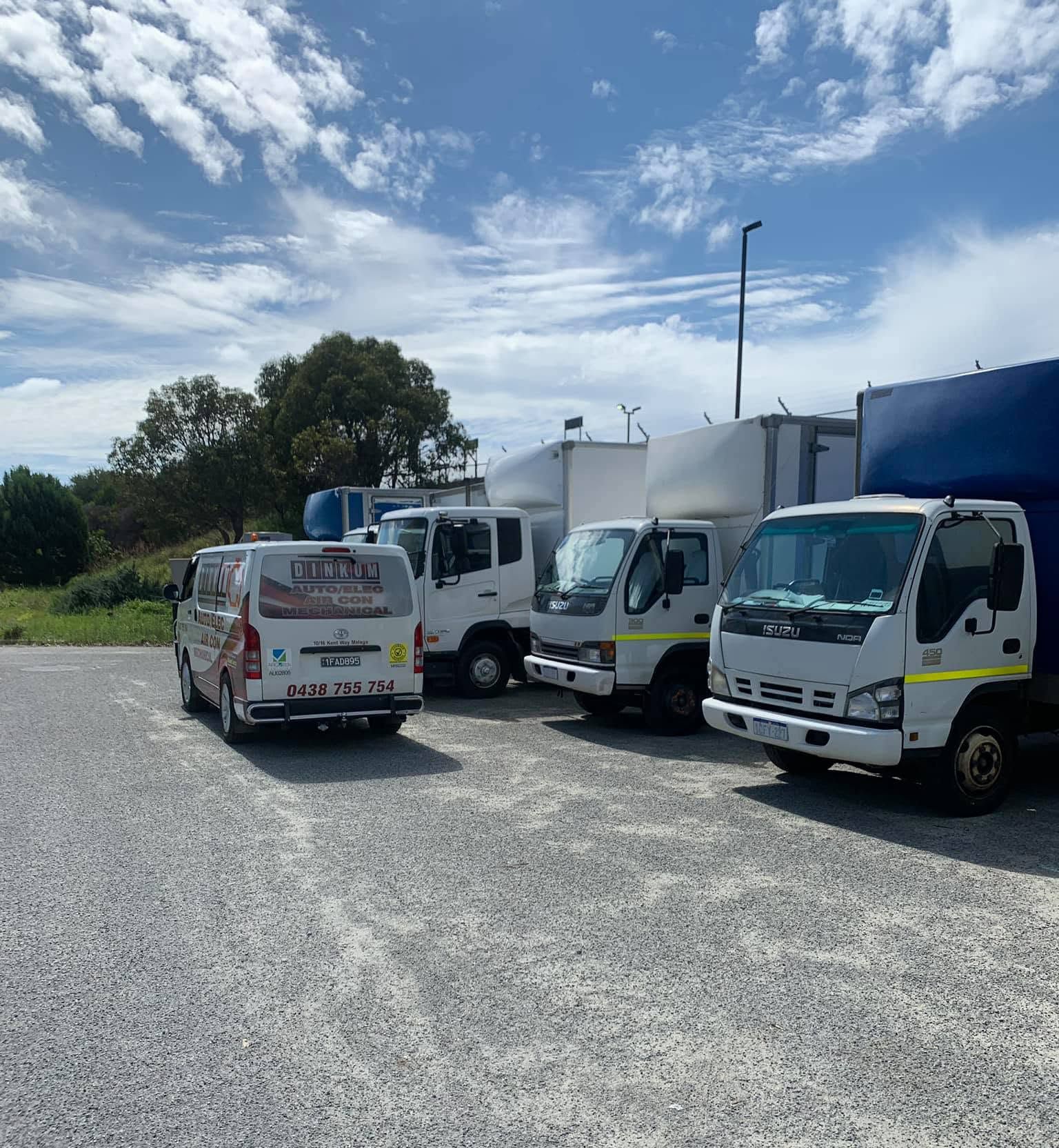 Several white delivery trucks parked on a gravel lot under a blue sky. Several white delivery trucks parked on a gravel lot under a blue sky.