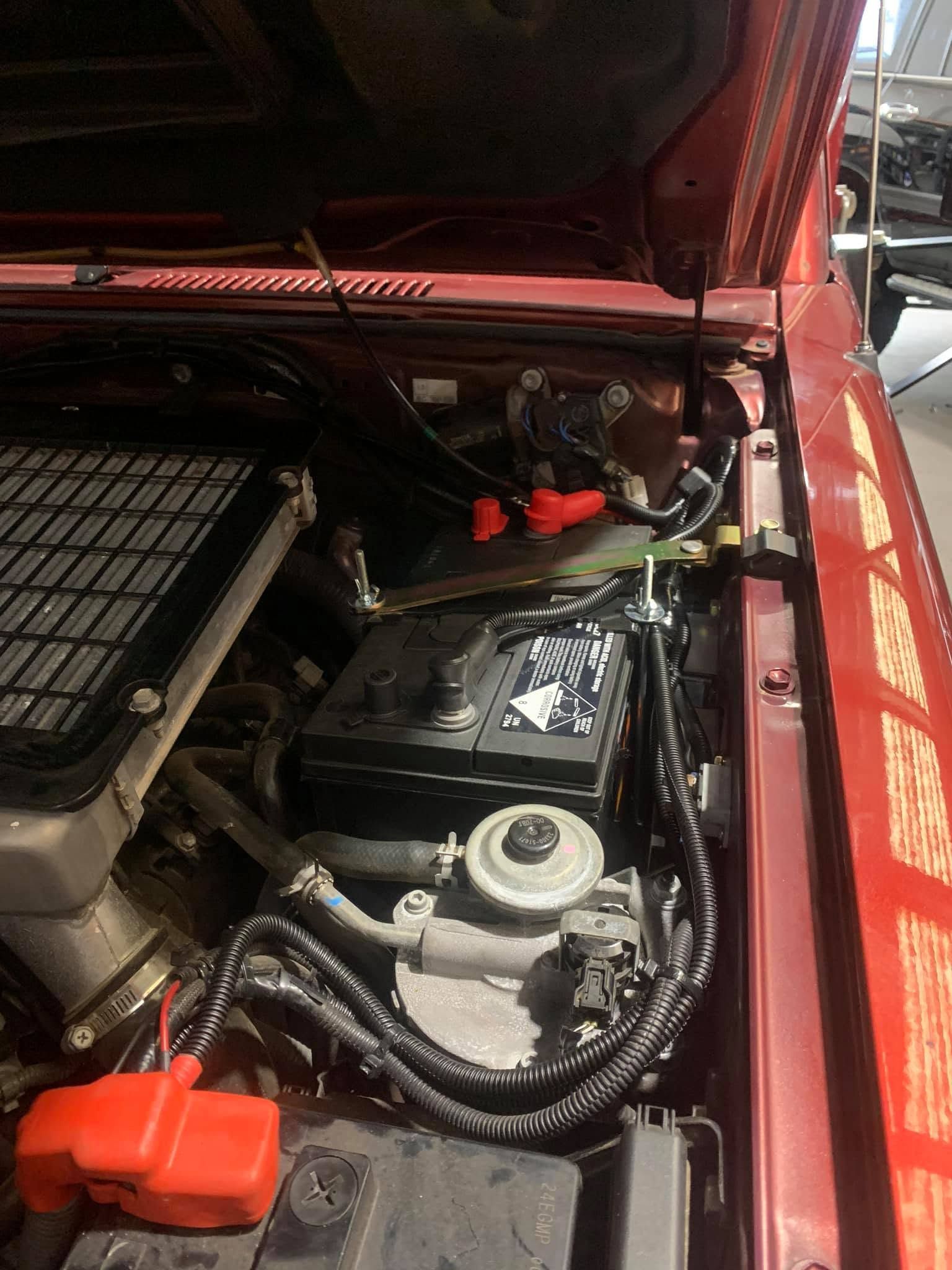 Open car hood showing a black engine bay with red battery cover and air filter box