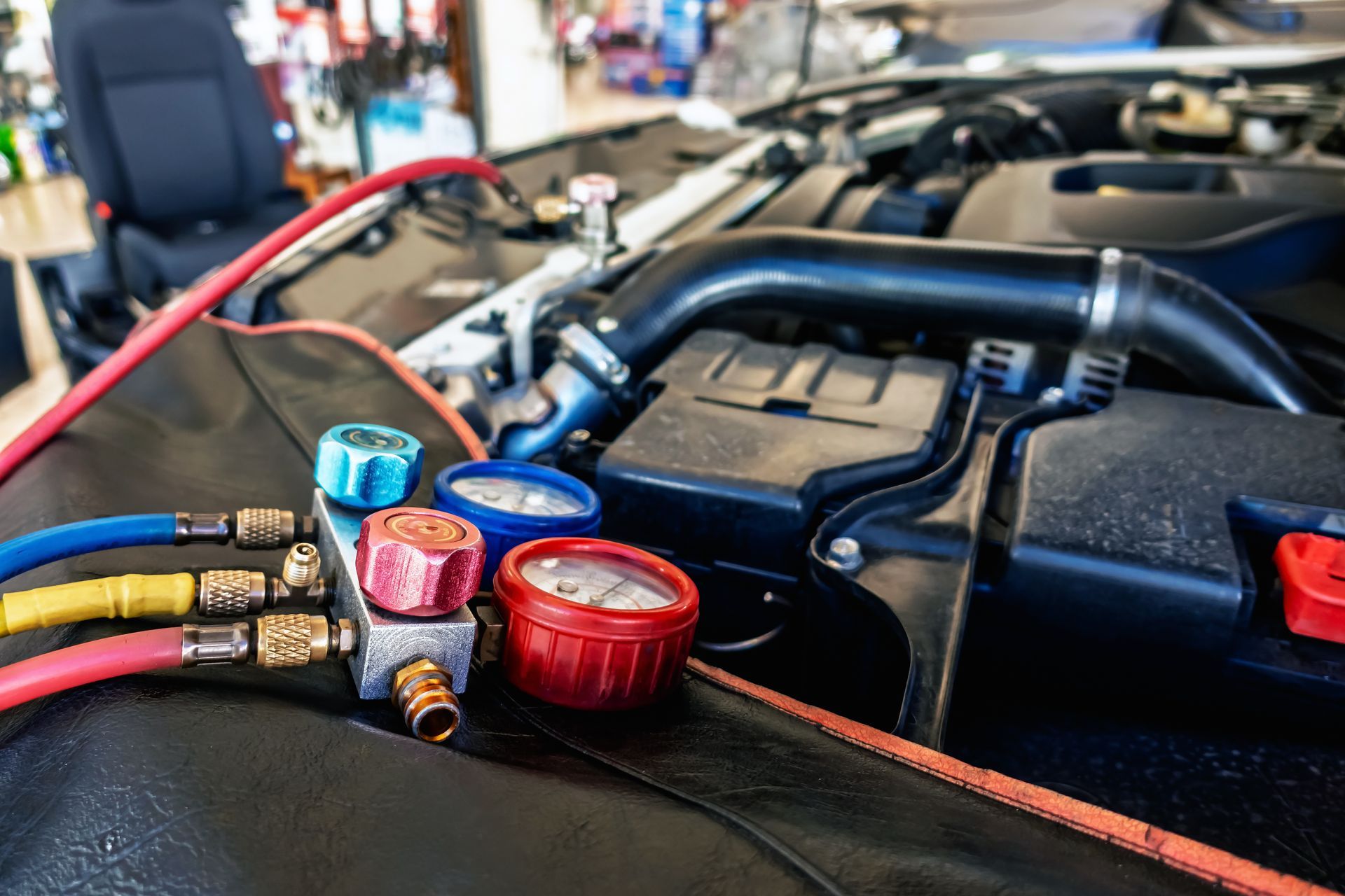 Car engine bay with colorful fluid caps and hoses, shown in a garage or workshop.