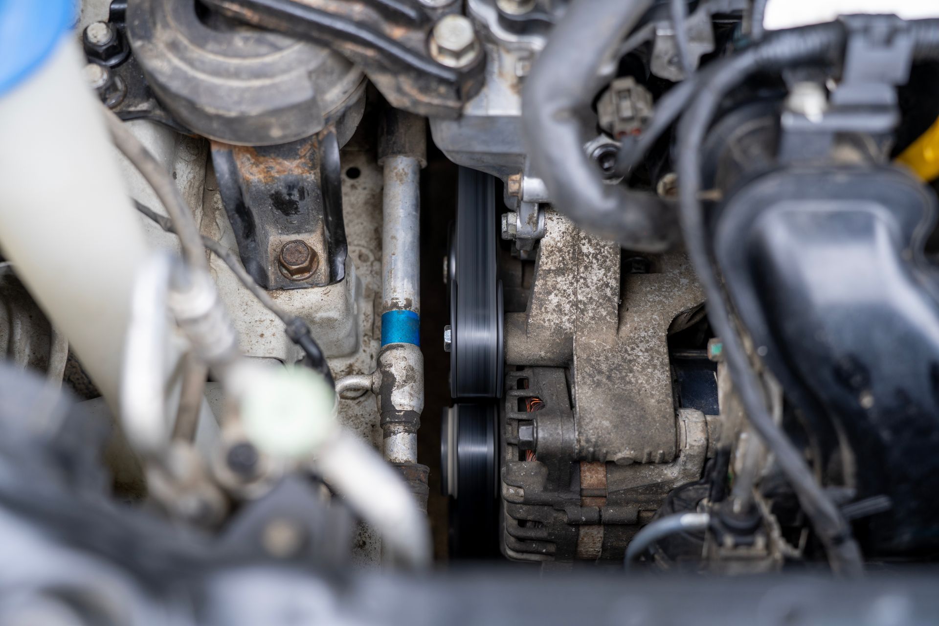 Close-up of a car engine belt and pulleys with surrounding hoses and metal components Close-up of a car engine belt and pulleys with surrounding hoses and metal components