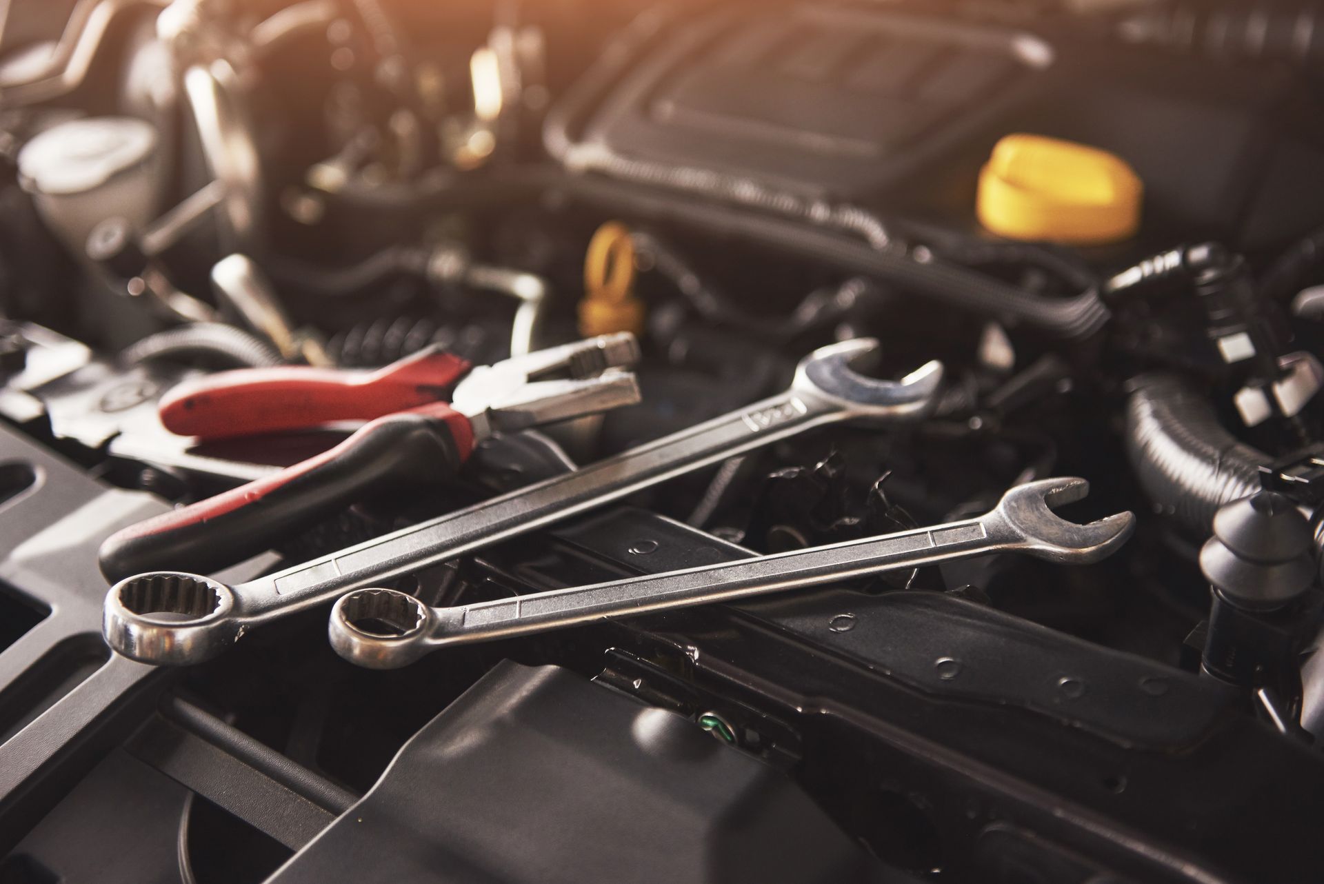 Assorted wrenches and pliers on a car engine, with a yellow cap in the background