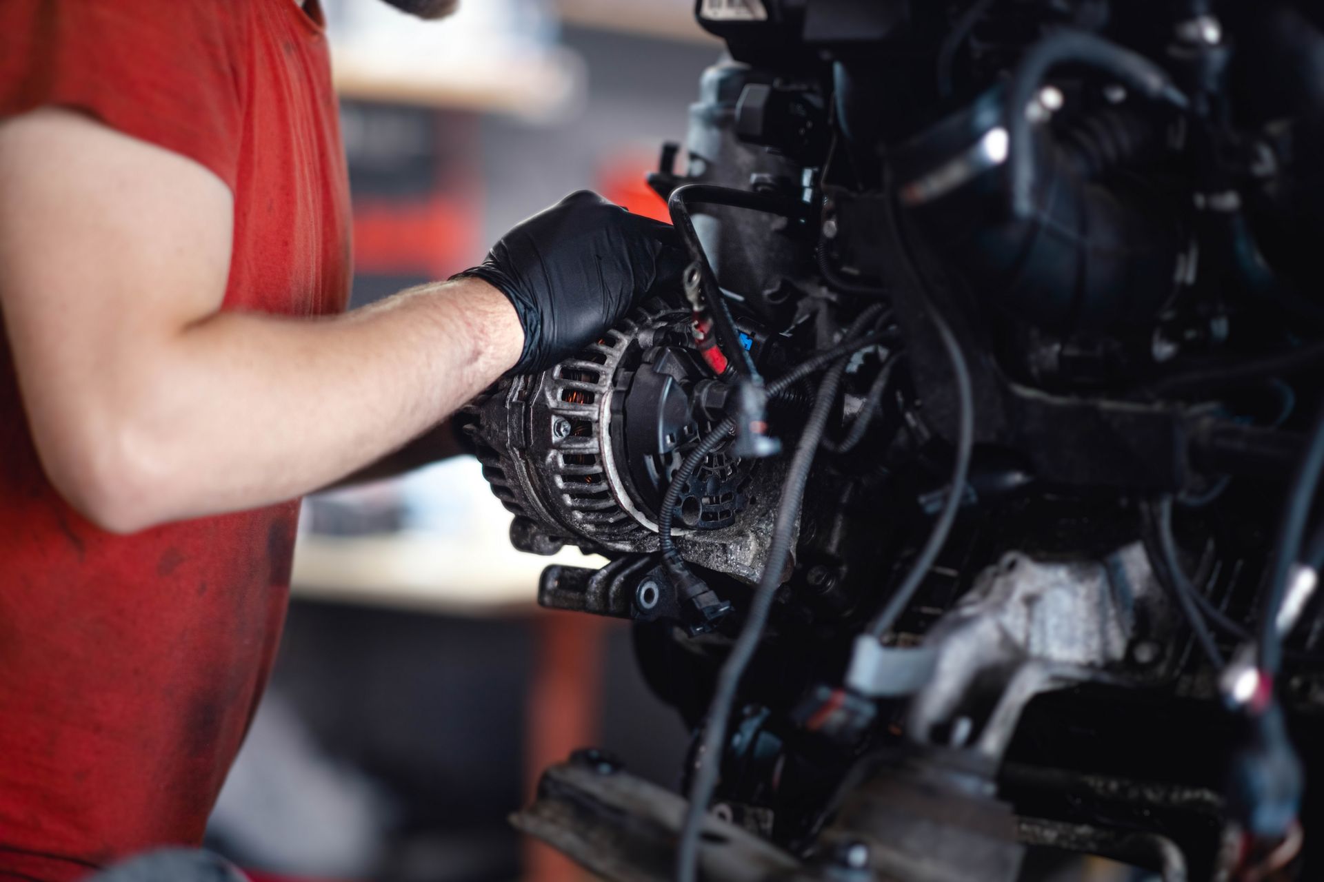 Mechanic in red shirt and black gloves working on a car engine with a wrench Mechanic in red shirt and black gloves working on a car engine with a wrench