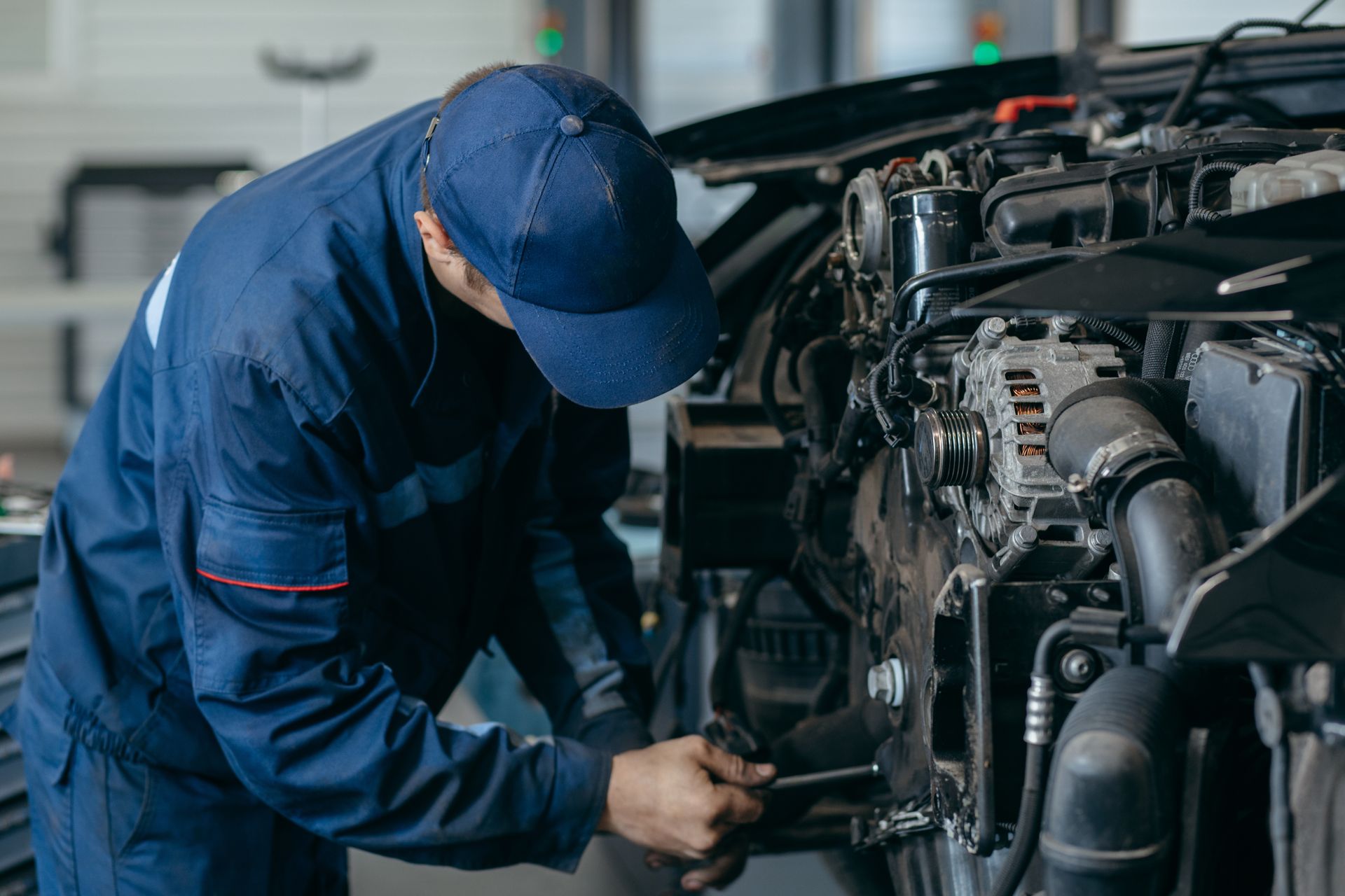 A uniformed mechanic wearing a cap carefully performs diesel engine diagnostics on an open engine.