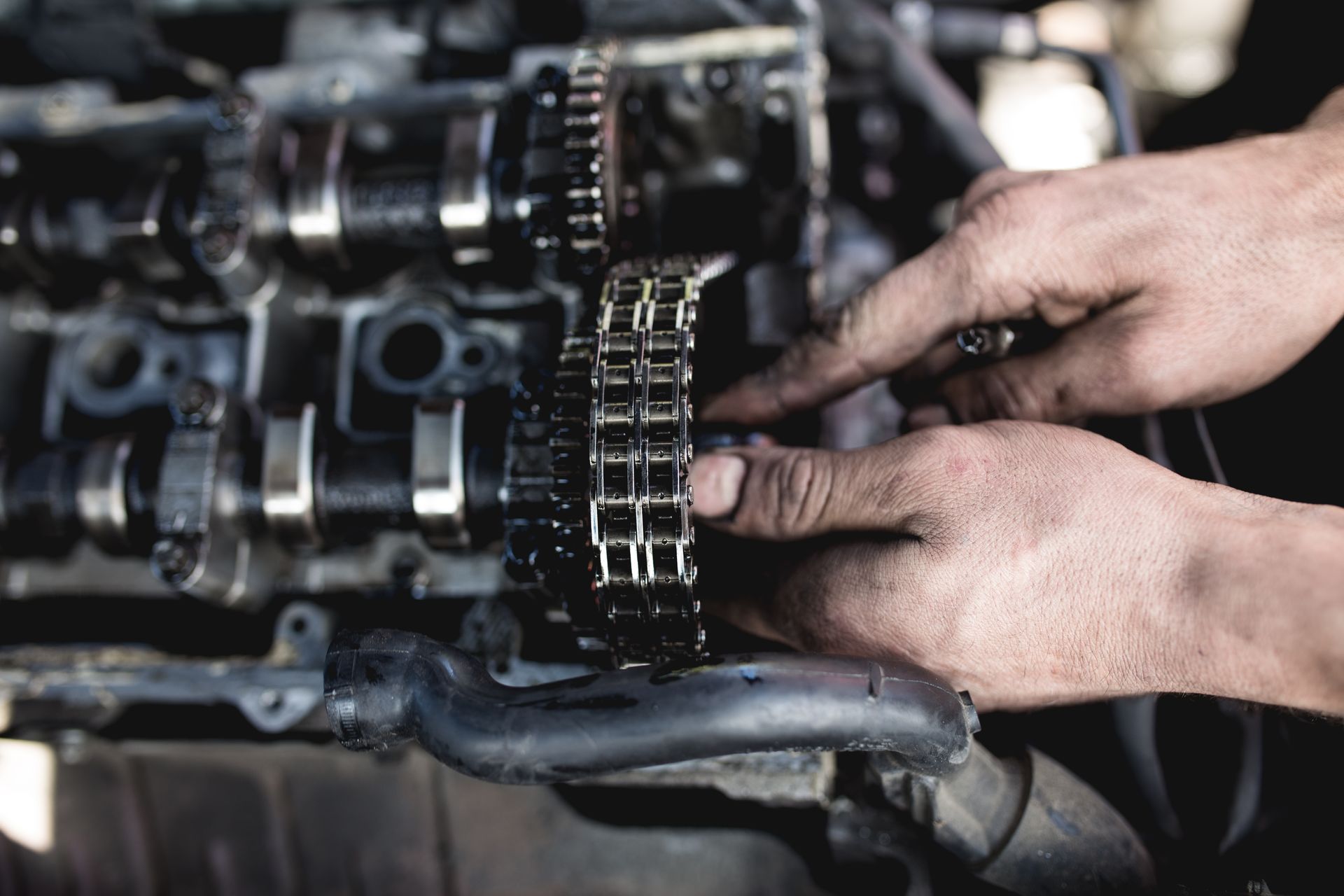 A technician's hands guide a greasy timing chain onto engine sprockets during diesel engine repair.