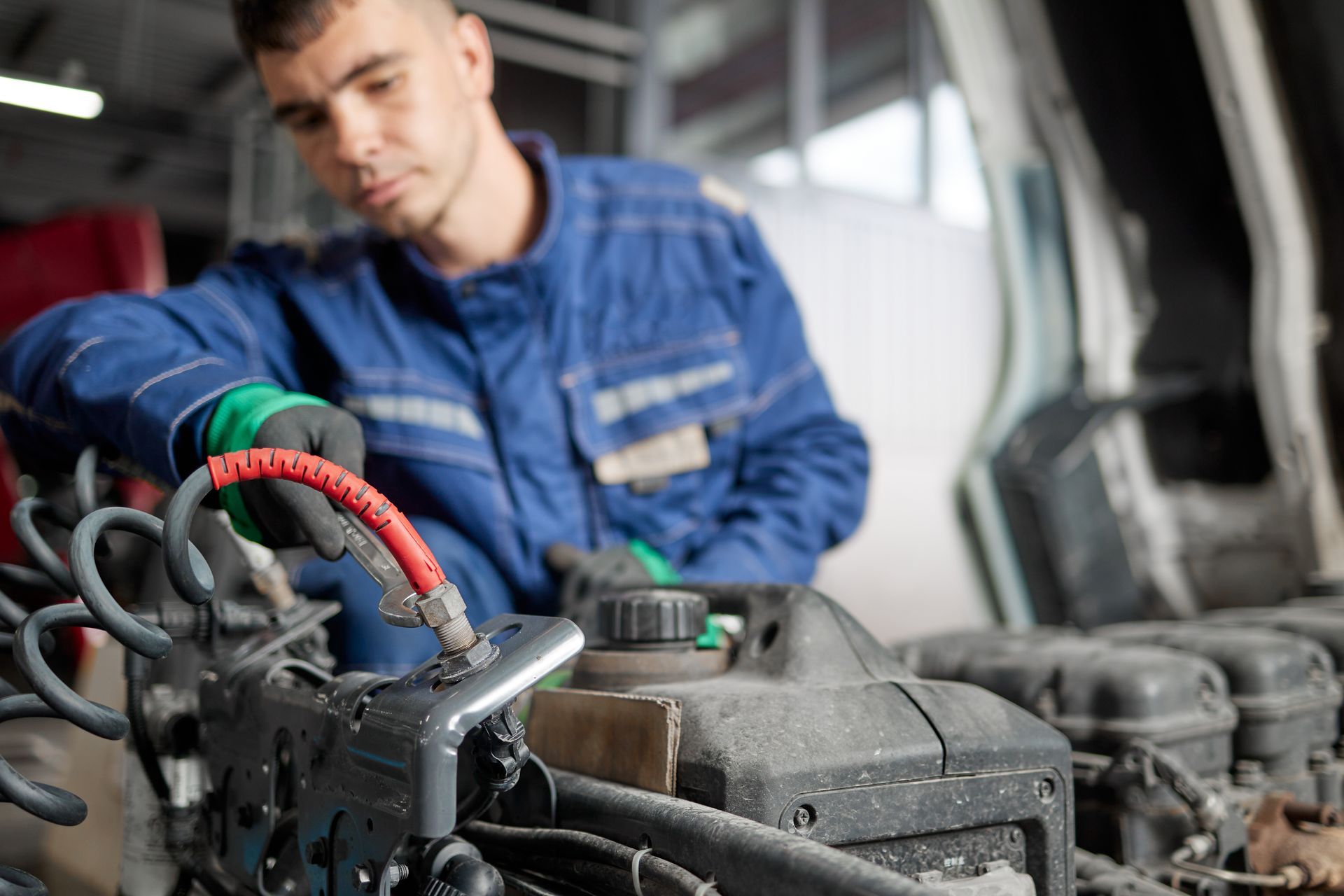Technician servicing a vehicle engine compartment inside an auto repair shop.