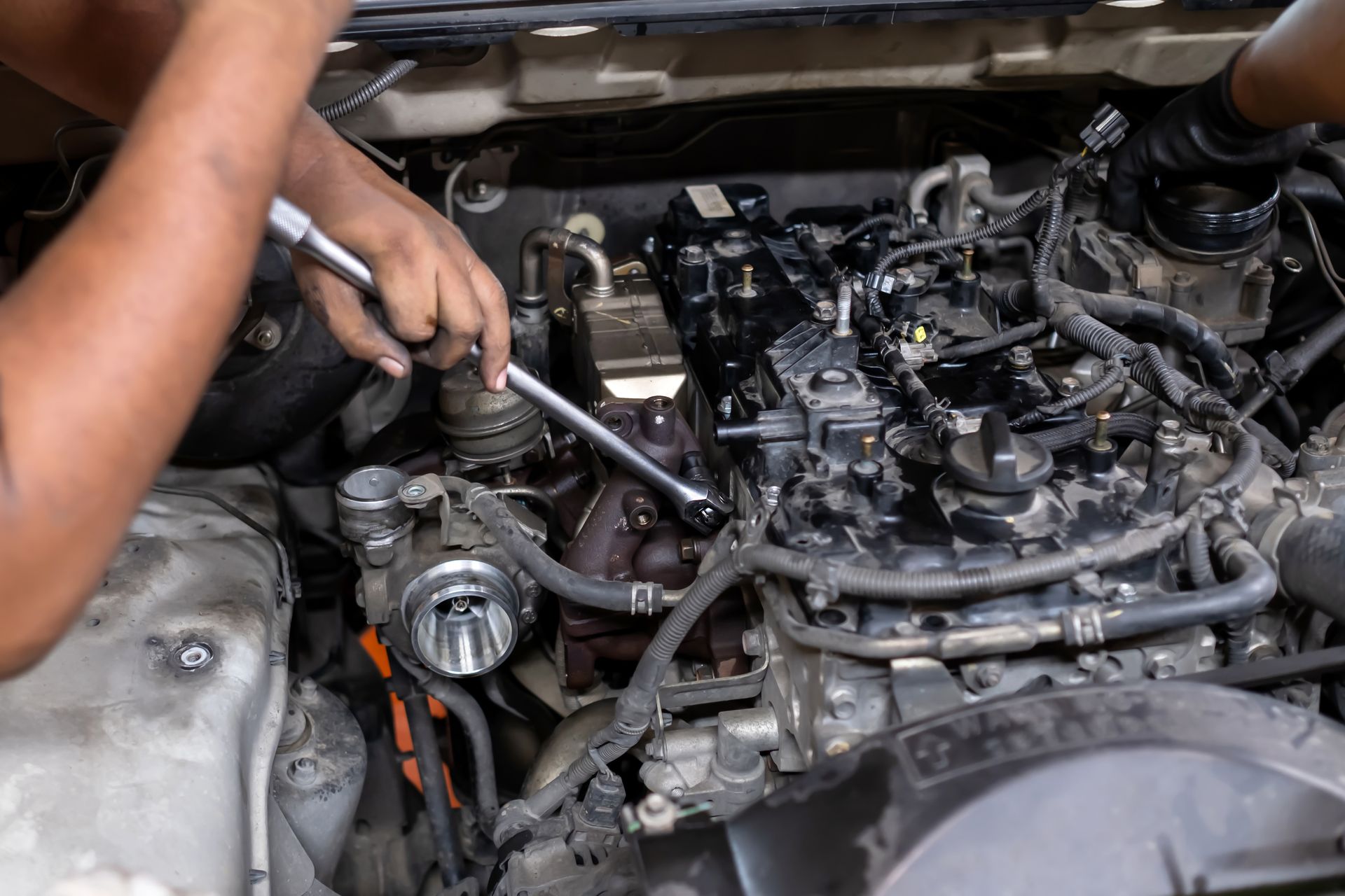Mechanic using a wrench to repair a car engine in an open hood bay