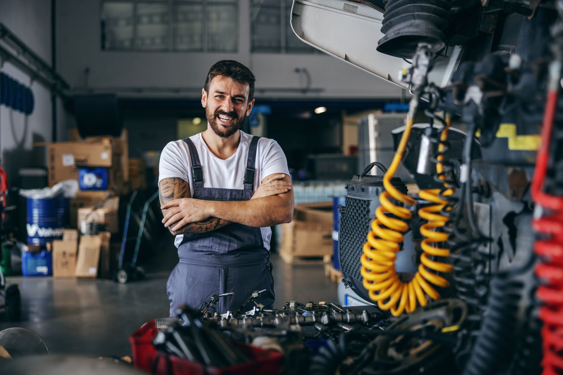Mechanic smiles, arms crossed, in a garage with tools and equipment.