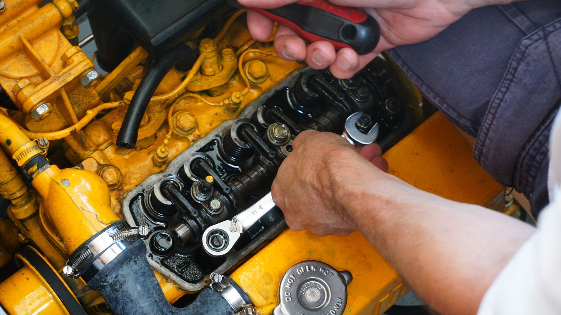 Hands using wrenches to repair and adjust components inside an engine