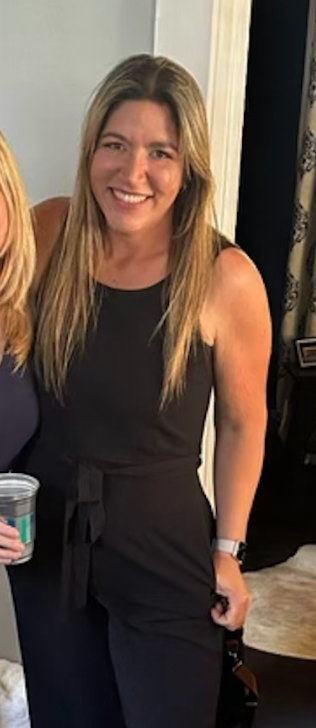 A woman in a black jumpsuit is smiling while standing next to two other women.